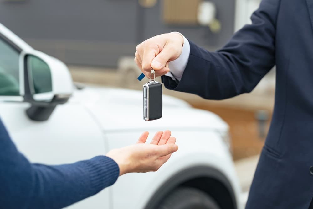 A man extending a smart car key symbolizes car rental or car sharing services, where individuals gain access to vehicles temporarily.